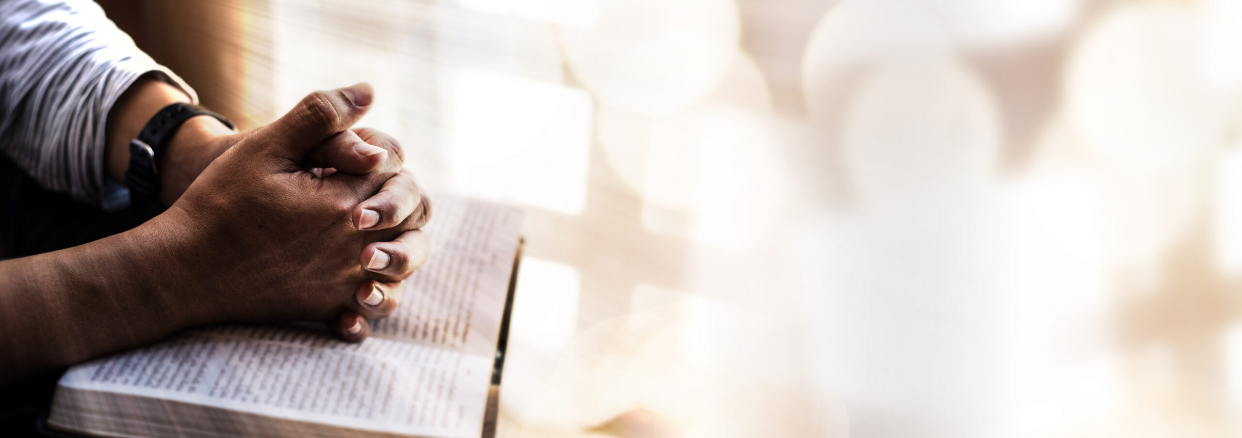 Hands folded on a bible, praying.